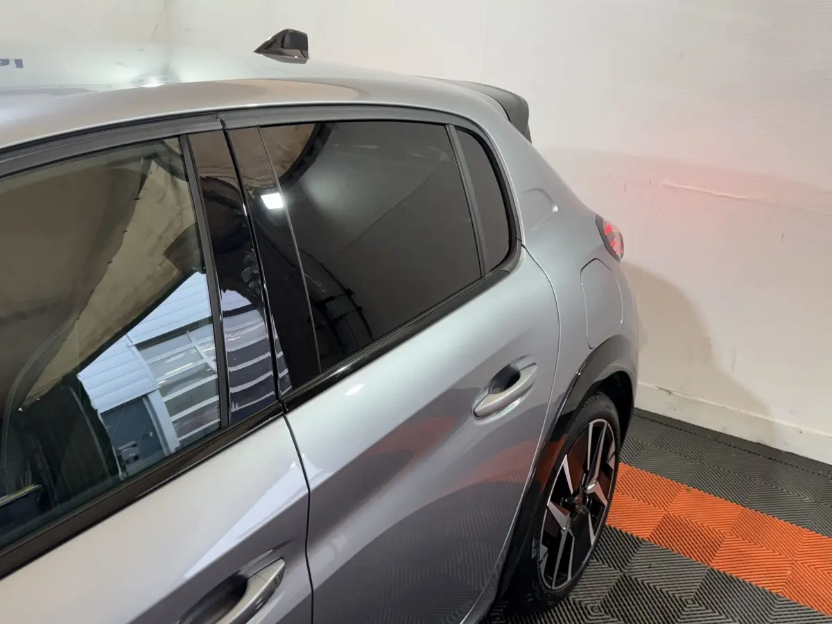 Vue côté droit arrière d'une Peugeot 208 Hybrid gris clair avec rétroviseur caméra et jante alliage noir et argent.