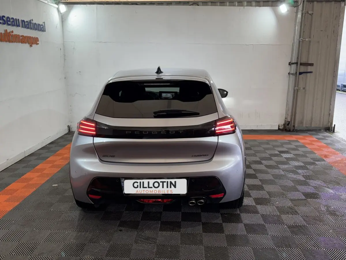 Vue arrière d'une Peugeot 208 Hybrid gris clair avec feux LED allumés dans un garage.