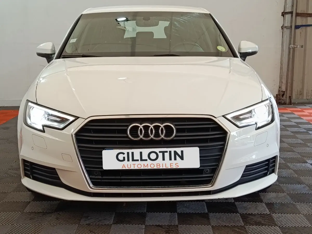 Vue avant d'une Audi A3 blanche de 2020 avec phares LED allumés et calandre noire distinctive.