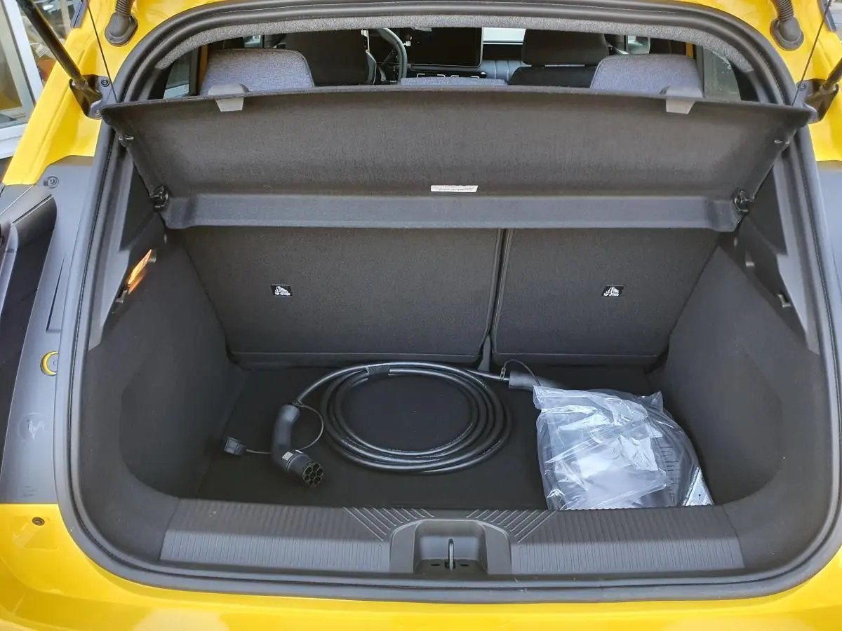 Coffre ouvert vu de l’arrière d’une Renault R5 E-Tech jaune Pop avec câble de recharge électrique visible.
