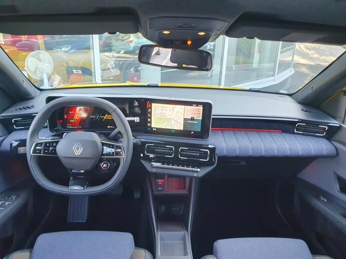 Vue intérieure avant du tableau de bord et volant de la Renault R5 E-TECH jaune avec écran tactile et éclairage d'ambiance rouge.