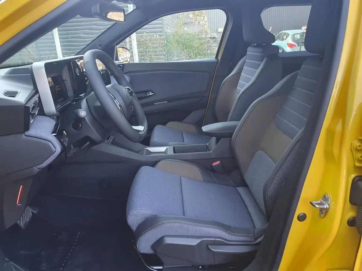 Vue intérieure côté conducteur de la Renault R5 E-Tech jaune pop, montrant sièges bi-matière et tableau de bord moderne.