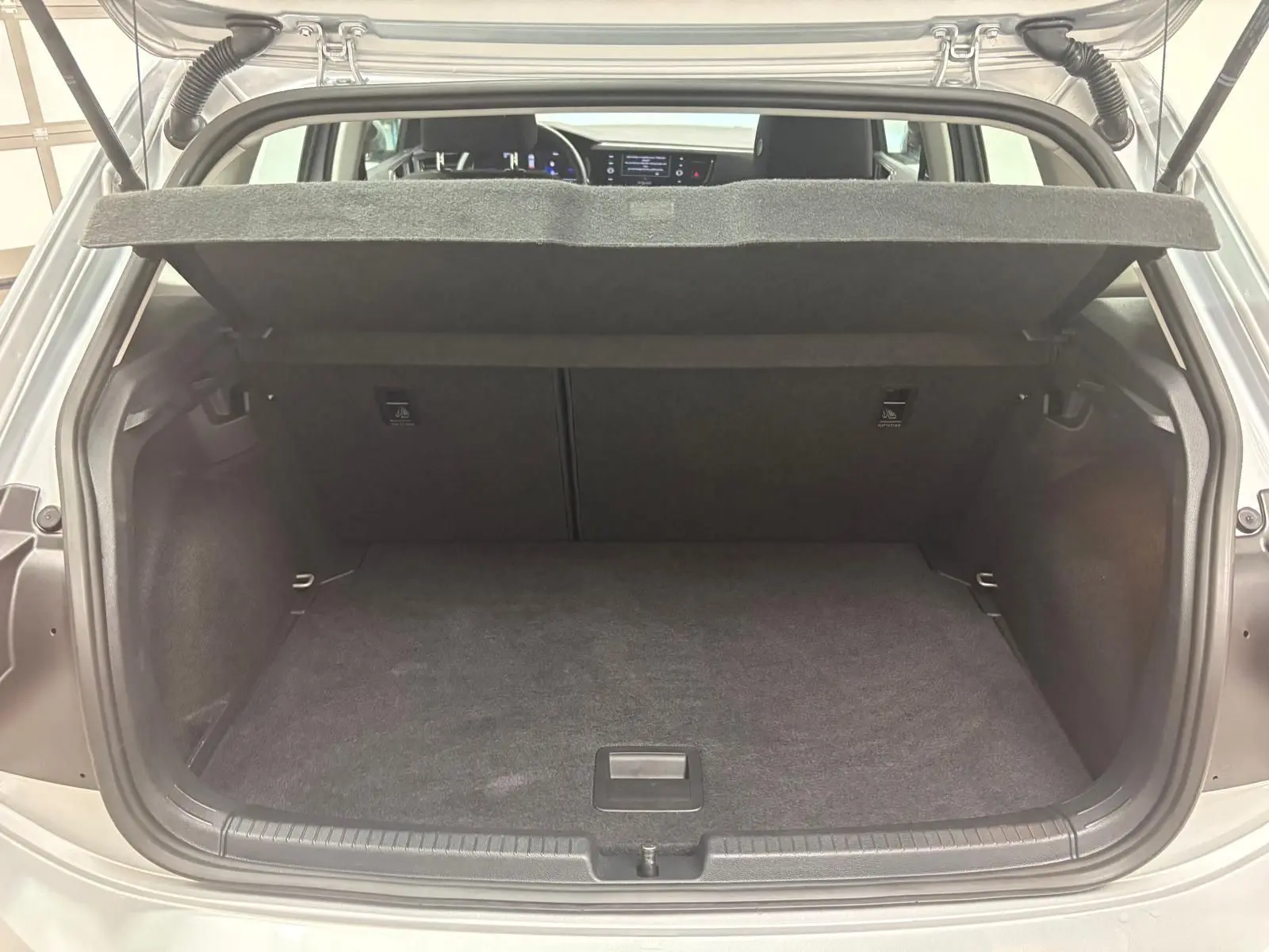 Coffre ouvert d'une Volkswagen Polo 2024 Reflet d'argent, vue arrière montrant l'espace de chargement vide et la tablette arrière relevée.