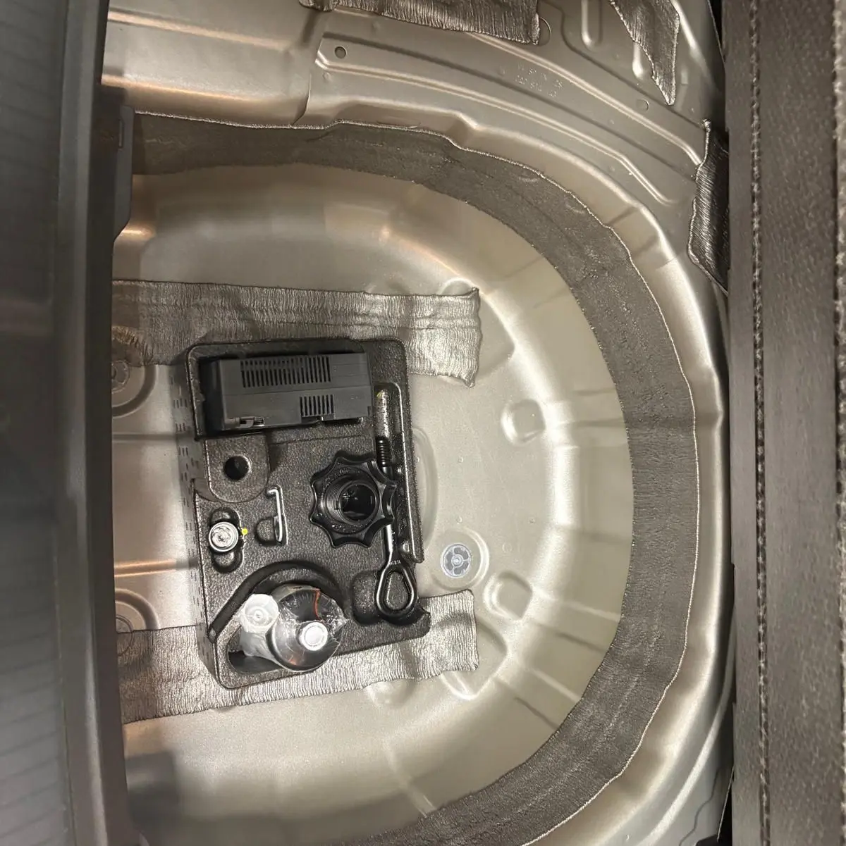 Vue rapprochée du coffre d'une Volkswagen Polo 2024 Reflet d'argent, montrant le logement de la roue de secours et l'outillage.