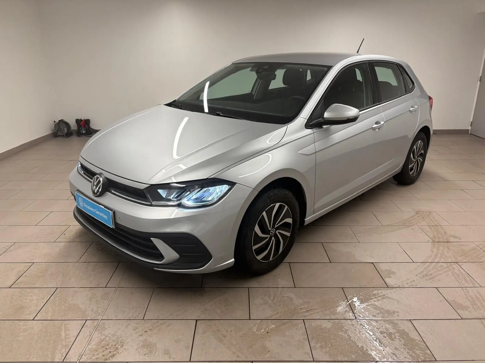 Volkswagen Polo 2024 couleur Reflet d'argent vue 3/4 avant droit avec phares allumés en intérieur.