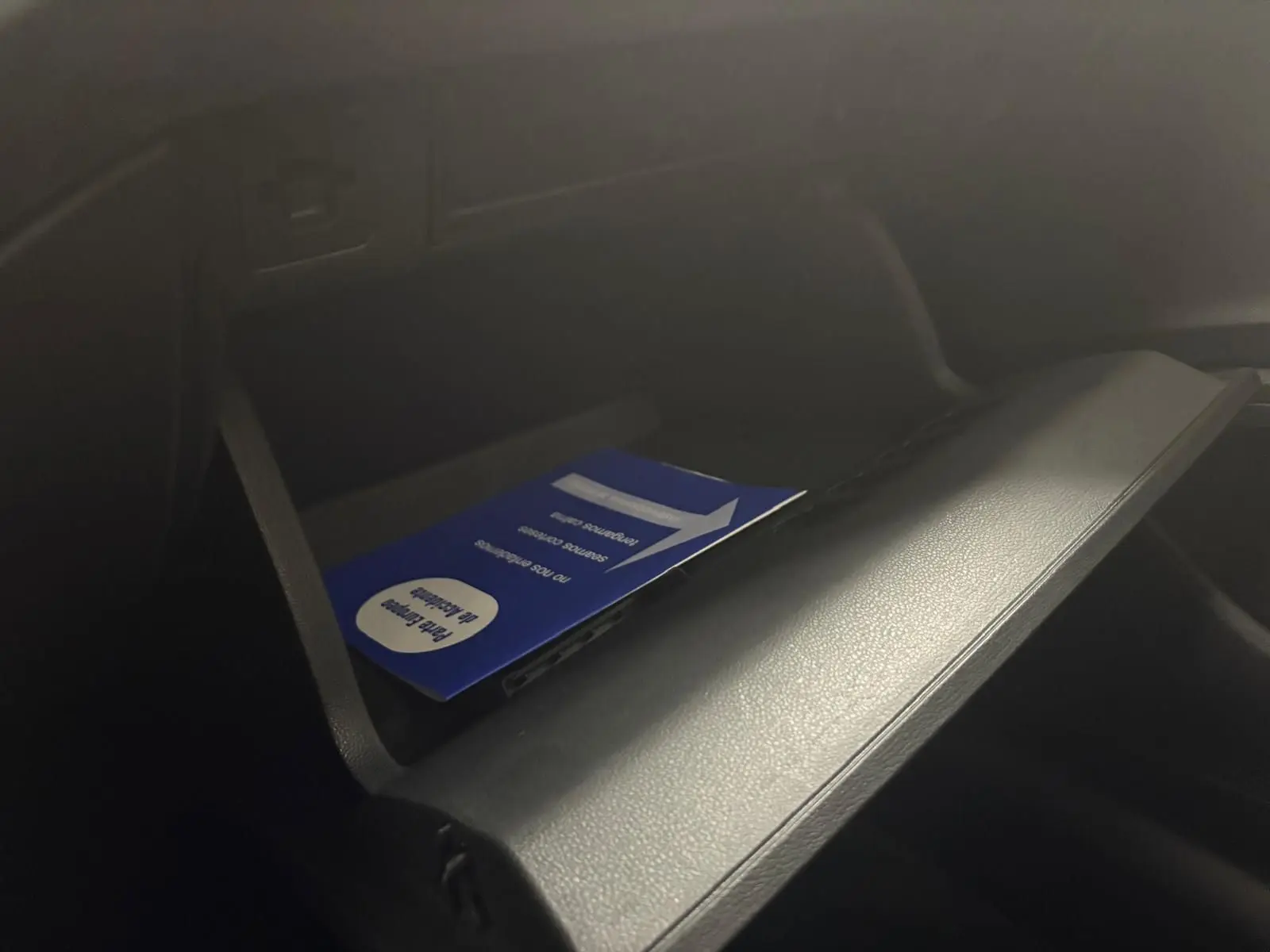 Gros plan sur la boîte à gants ouverte de la Volkswagen Polo 2024 avec un manuel bleu à l'intérieur, intérieur noir.