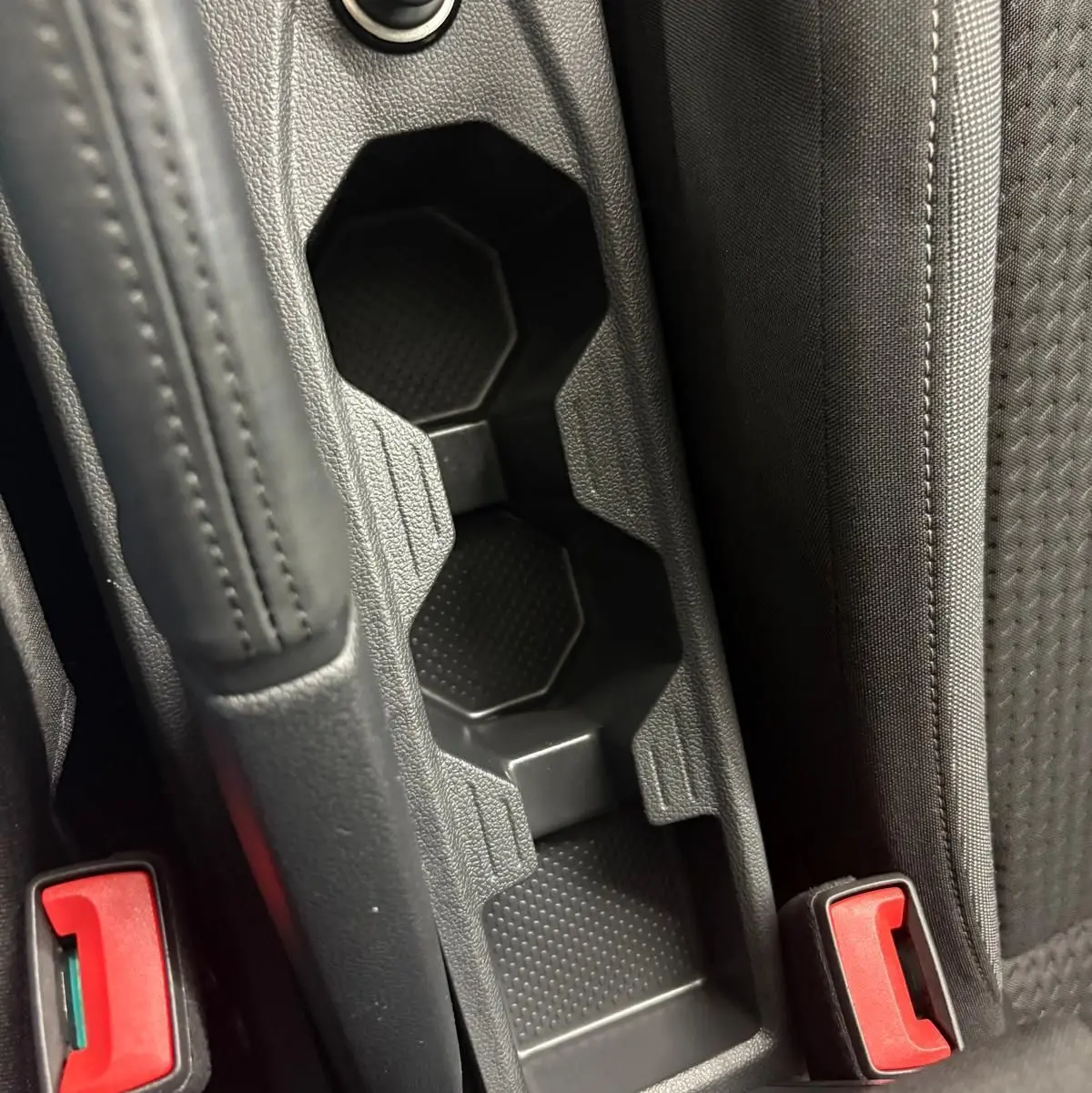 Gros plan sur la console centrale noire avec porte-gobelets et bouton 12V dans une Volkswagen Polo 2024.