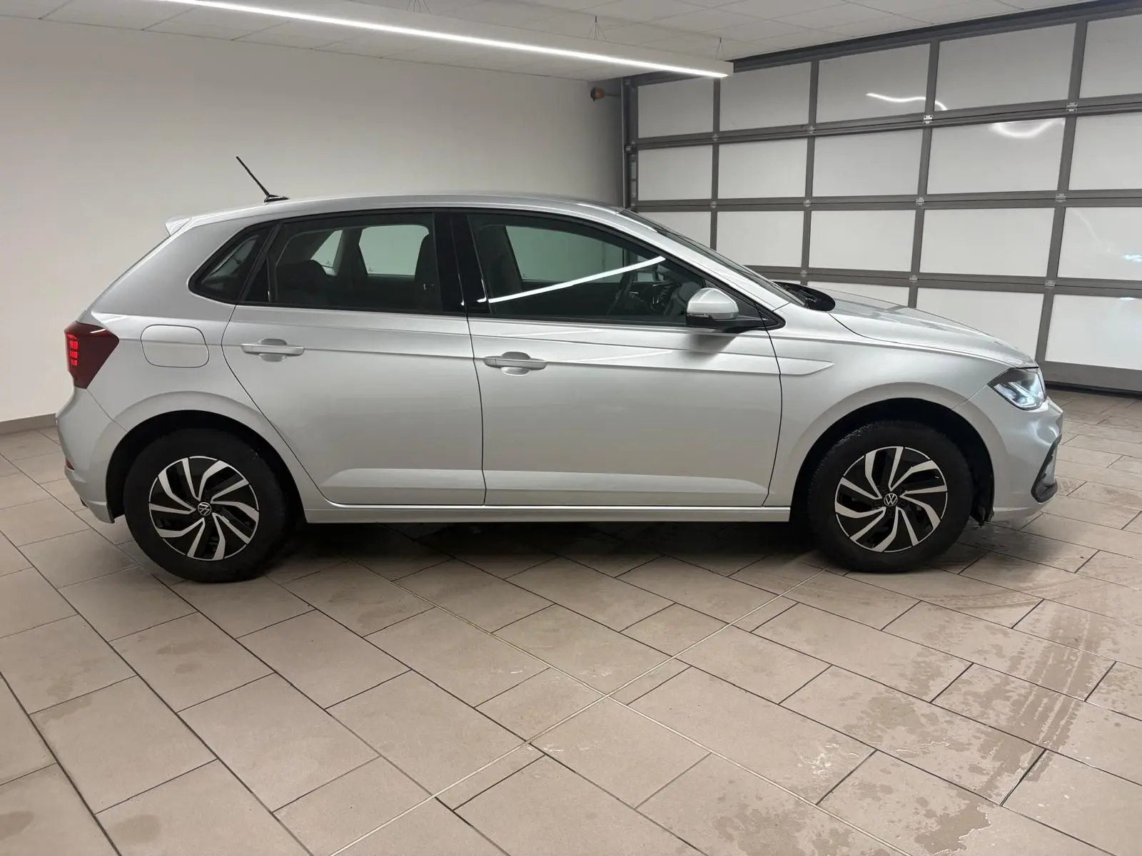 Profil droit d'une Volkswagen Polo 2024 en peinture métallisée Reflet d'argent, avec jantes au design moderne et caméra de recul visible.