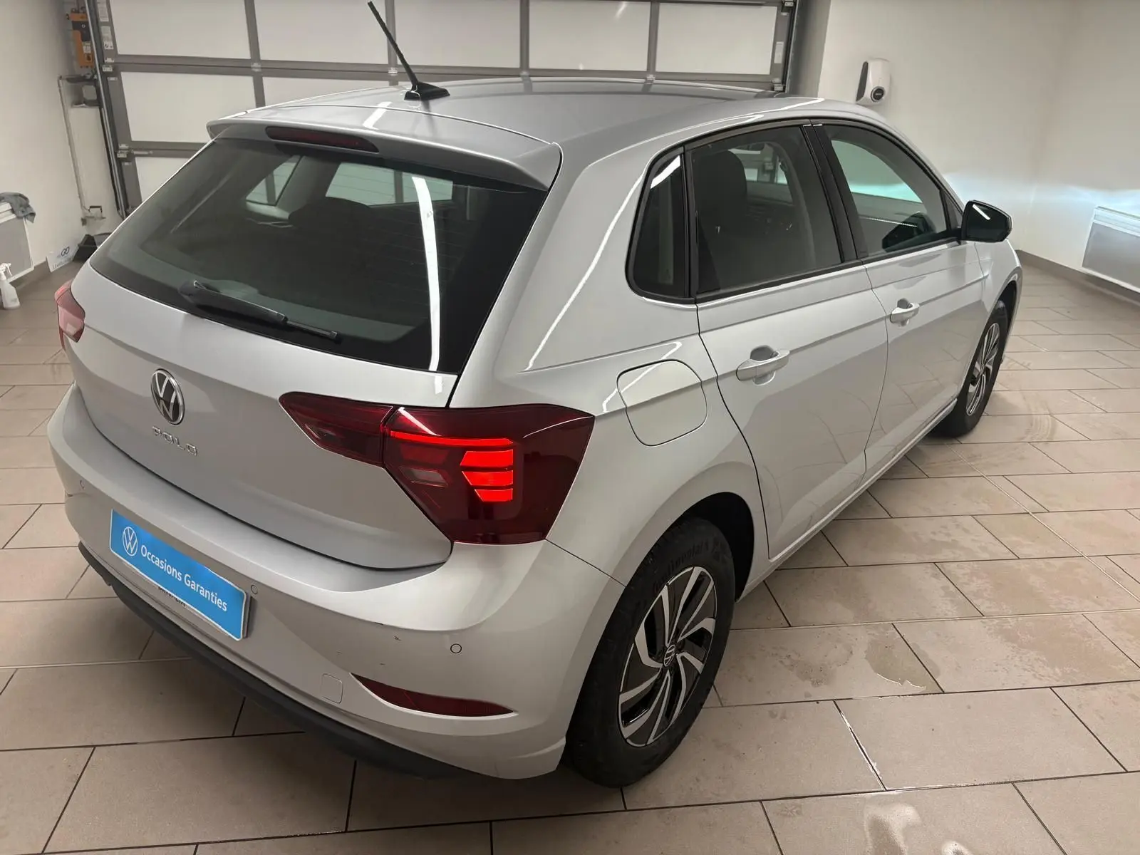 Volkswagen Polo 2024 argent métallisé vue 3/4 arrière droit avec feux arrière allumés en intérieur showroom.