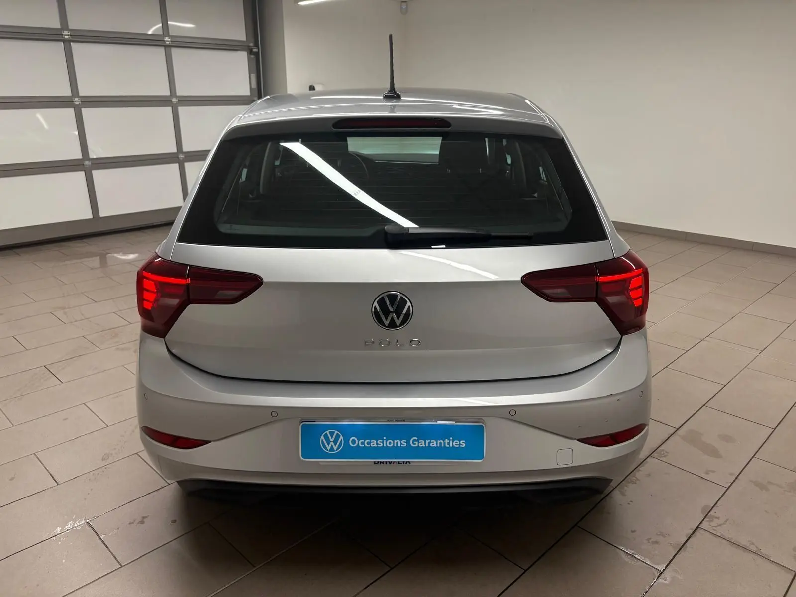 Vue arrière d'une Volkswagen Polo 2024 en peinture métallisée Reflet d'argent avec feux arrière allumés dans un garage.
