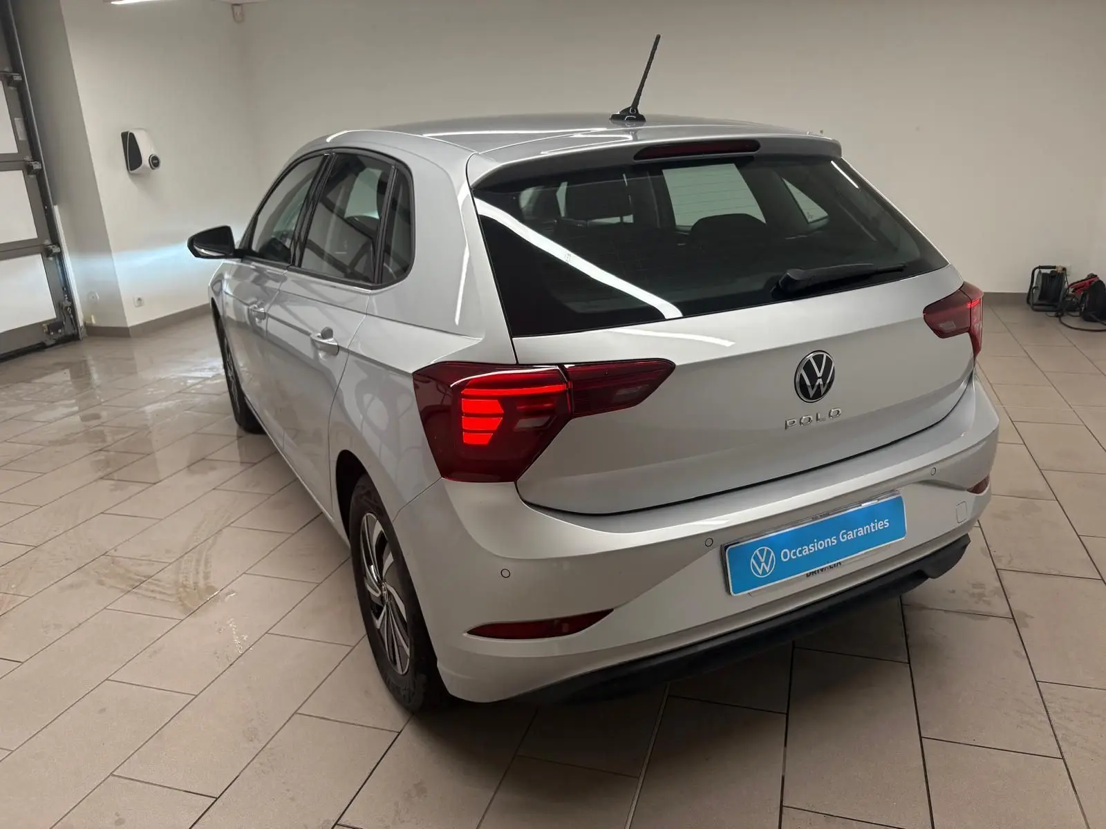 Volkswagen Polo 2024 argent métallisé vue 3/4 arrière droit en intérieur avec feux arrière allumés.