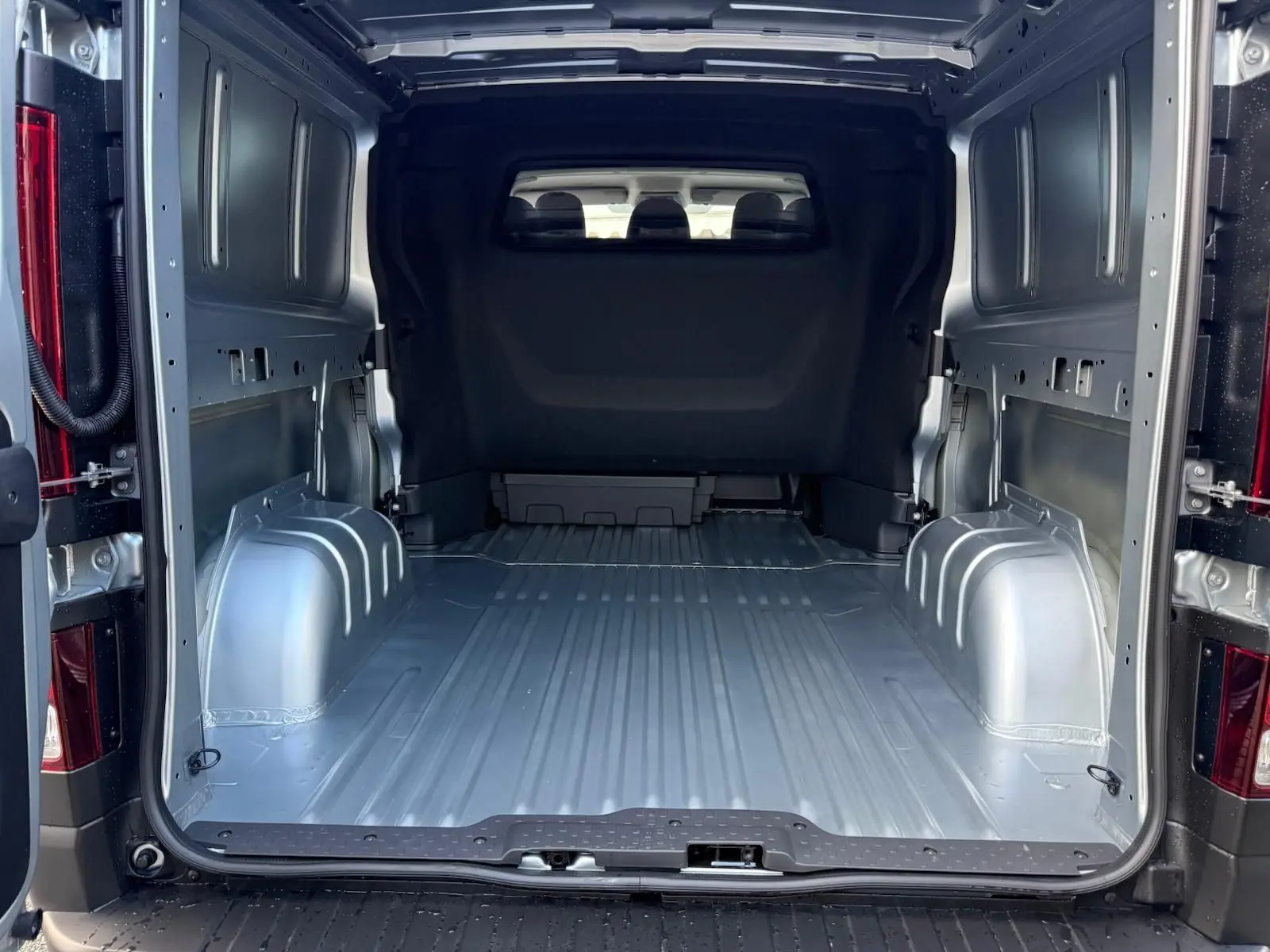 Vue 3/4 arrière droite d'un Renault Trafic cabine approfondie gris Highland avec vitres teintées et feux arrière verticaux.