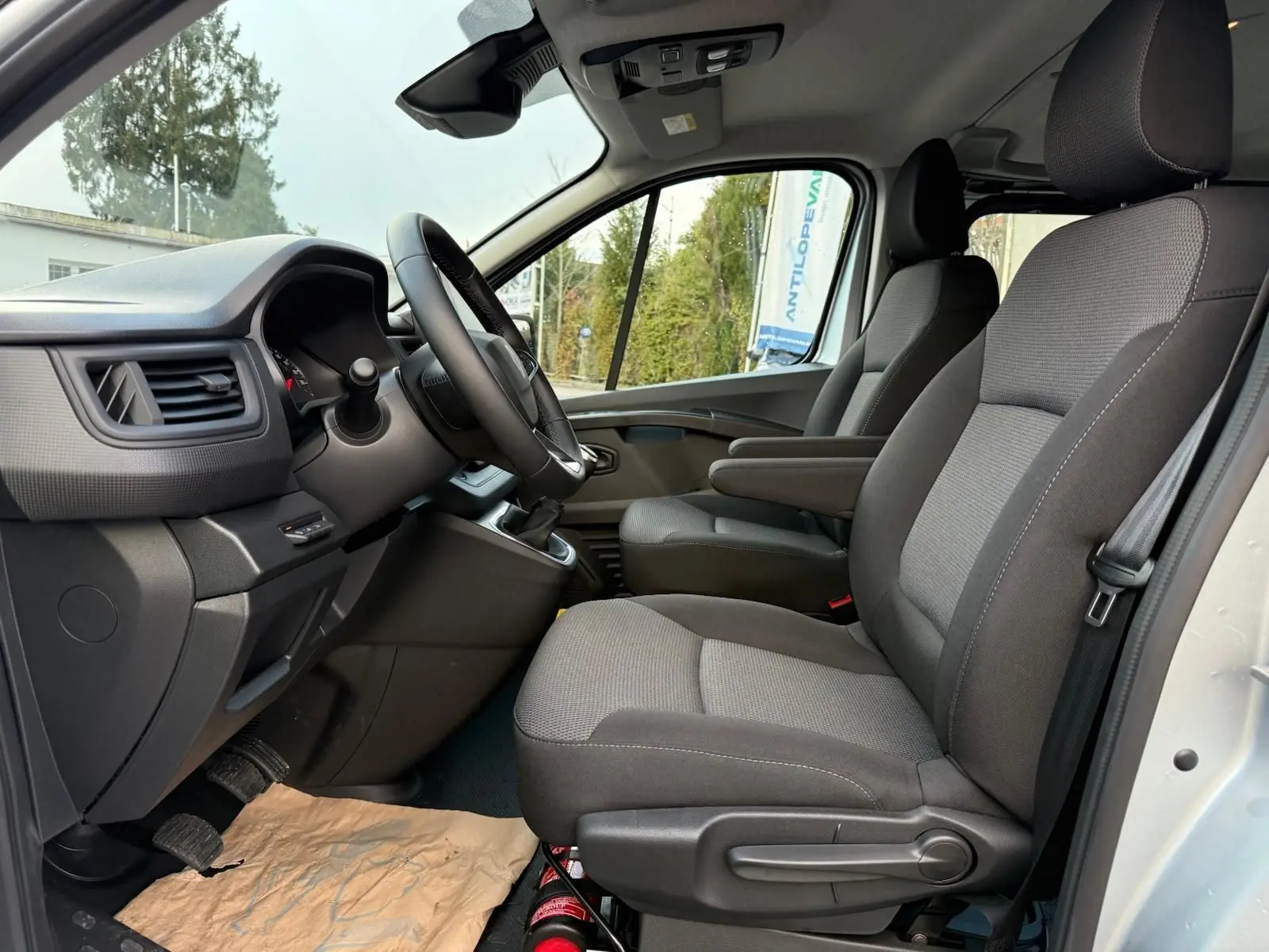 Vue intérieure côté conducteur du Renault Trafic cabine approfondie 2025, sièges gris et tableau de bord noir.