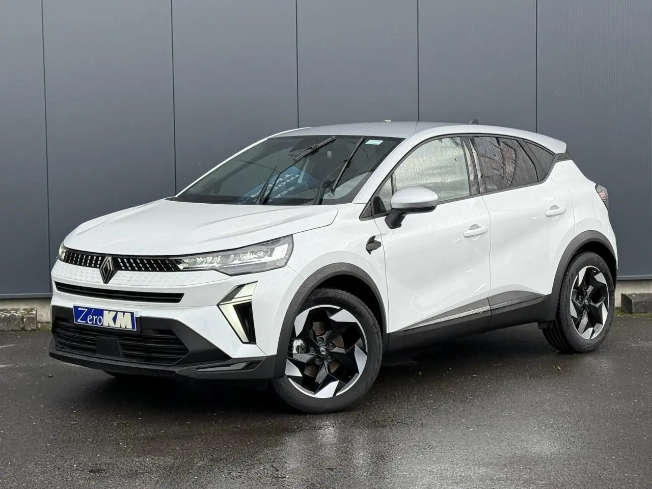Renault Captur 2025 blanc nacré en 3/4 avant droit avec jantes noires et toit gris Highland visible.