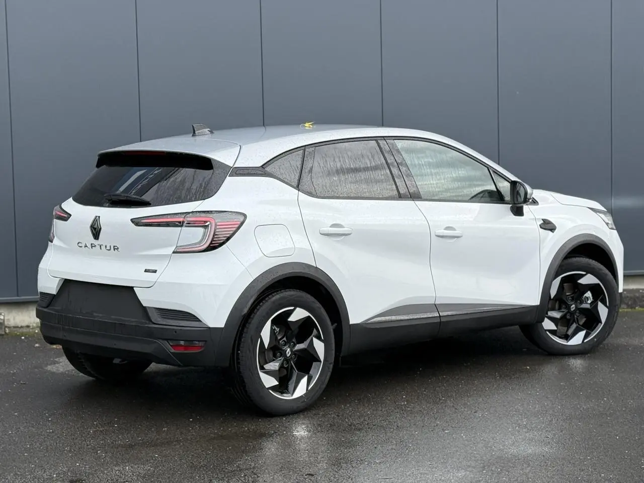 Renault Captur hybride 2025 blanc nacré vue 3/4 arrière côté droit avec toit gris et jantes noires.