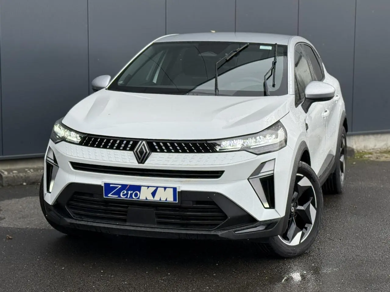 Vue 3/4 avant d’un Renault Captur blanc nacré avec toit gris Highland et jantes noires sur parking.