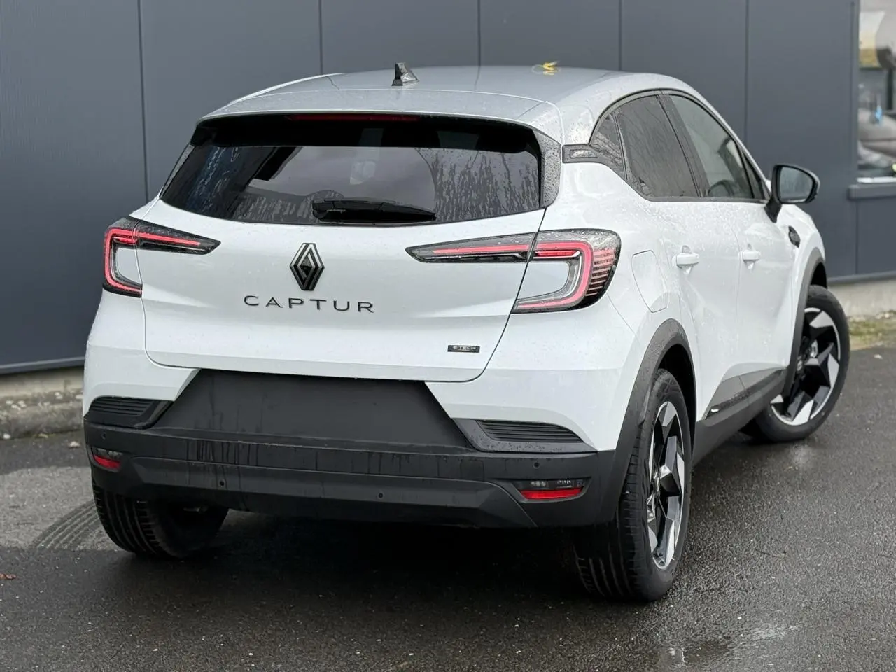 Vue 3/4 arrière droite d'un Renault Captur blanc nacré avec toit gris Highland et jantes noires 18 pouces.