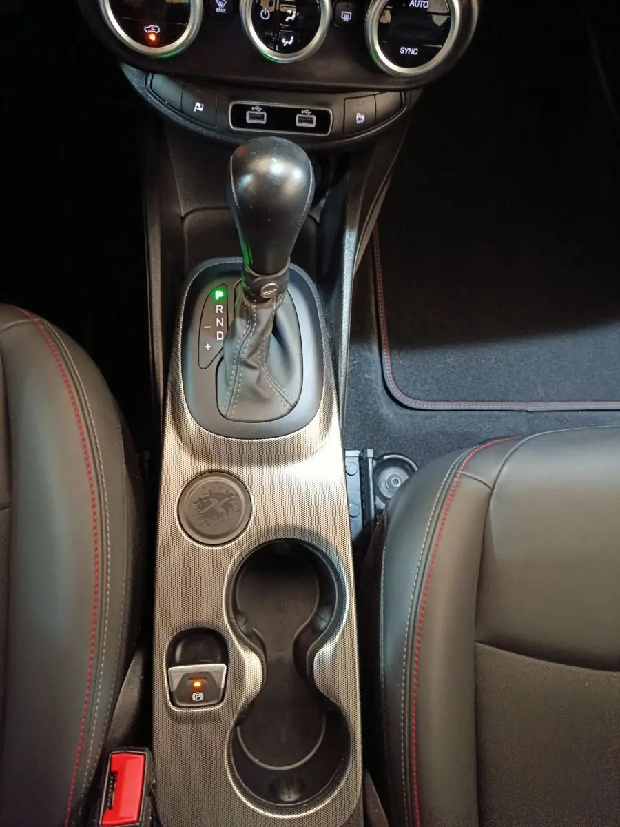 Vue plongeante sur la console centrale noire de la FIAT 500X 2021 avec levier de boîte auto et surpiqûres rouges.