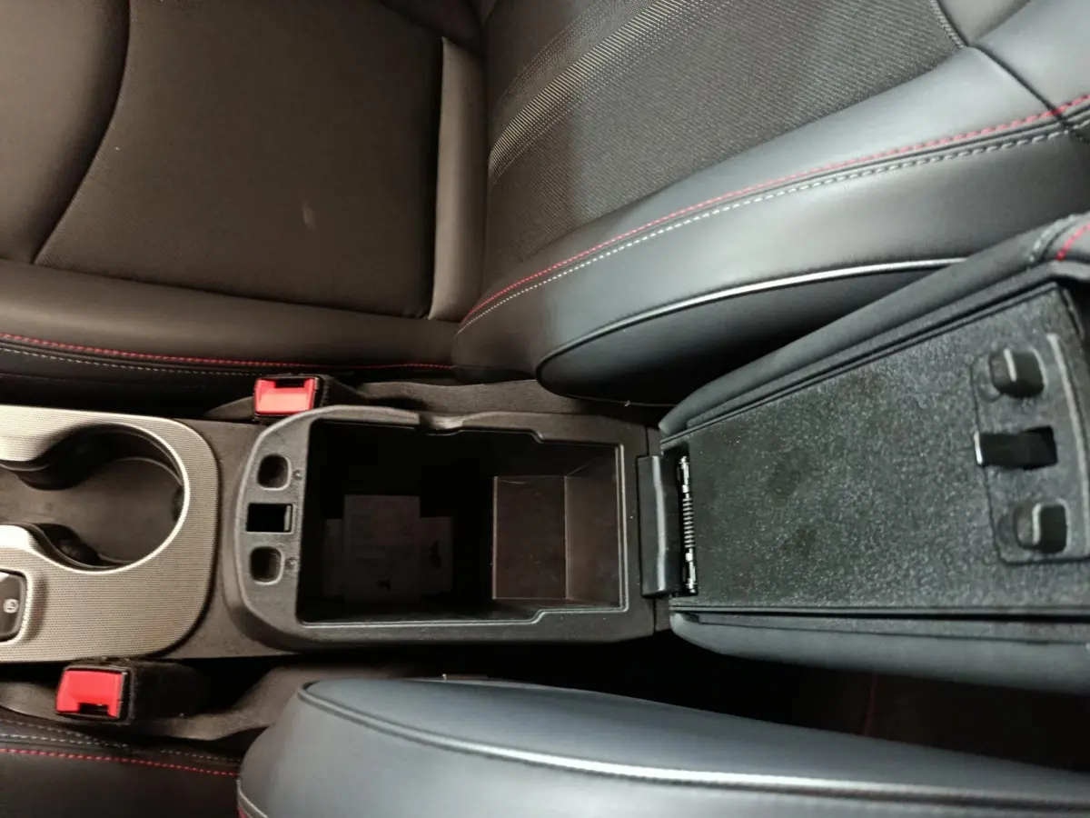 Vue rapprochée de la console centrale ouverte avec accoudoirs noirs et surpiqûres rouges dans un Fiat 500X noir.