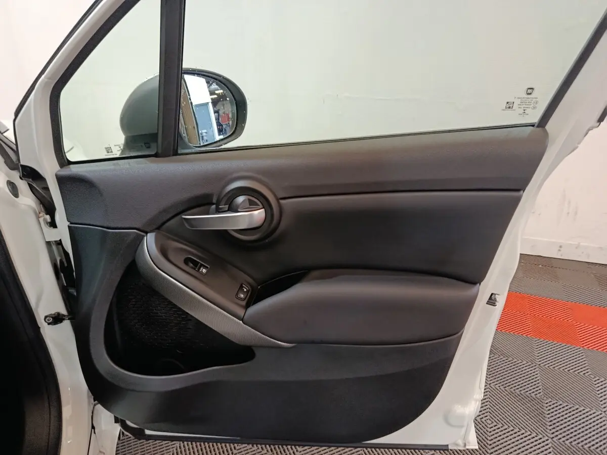 Vue intérieure de la porte avant gauche noire d'une FIAT 500X 2021 avec poignée argentée et commandes de vitres.