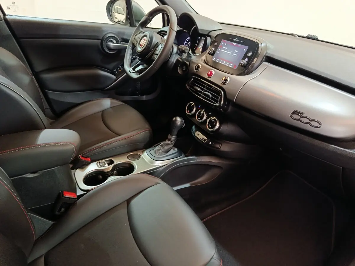 Vue intérieure côté conducteur de la FIAT 500X noire, avec tableau de bord moderne et écran tactile central.