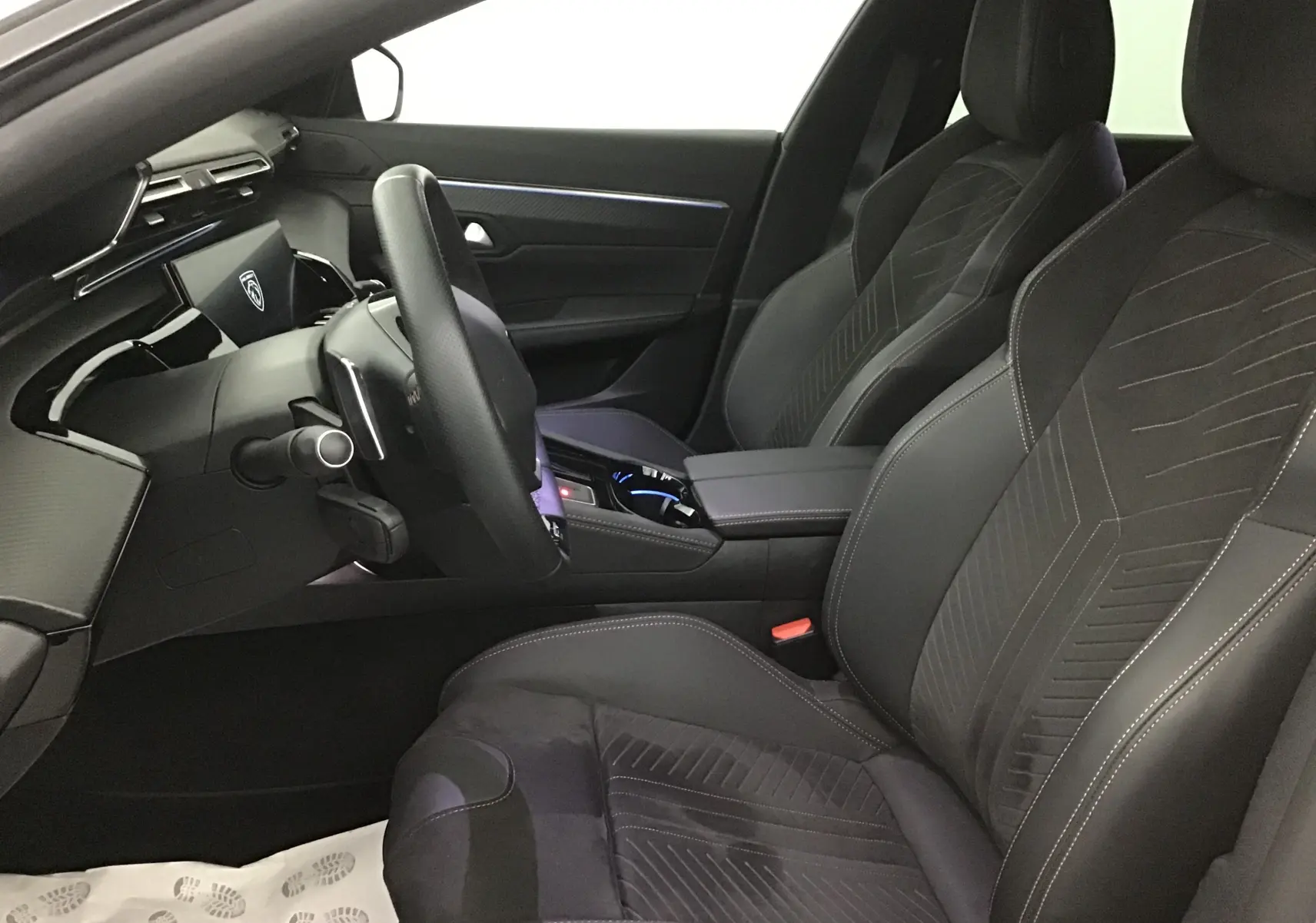 Intérieur avant droit du Peugeot 508 SW 2024 gris Artense, sièges sport noirs avec surpiqûres blanches et tableau de bord moderne.