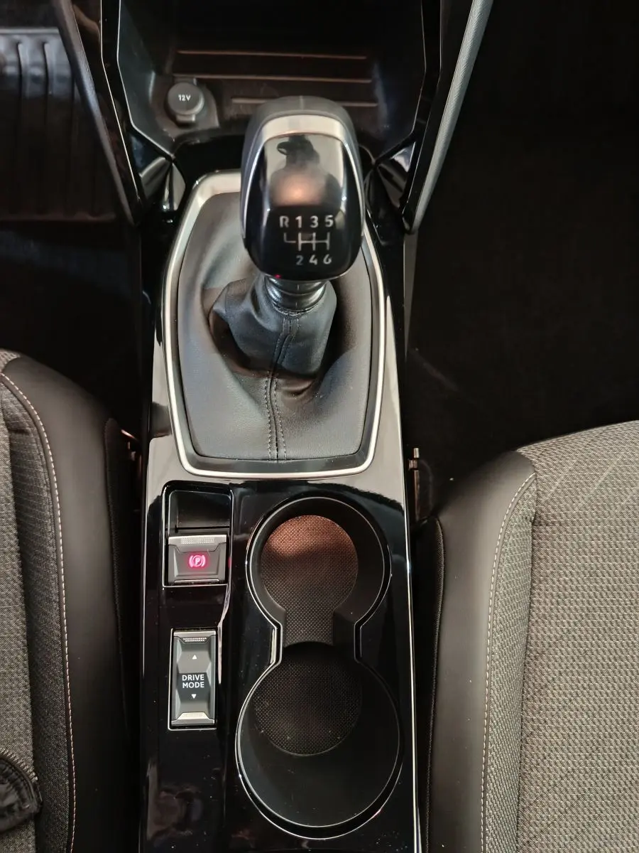 Vue plongeante sur la console centrale noire de la Peugeot 208 PureTech 100, avec levier de vitesses manuel et porte-gobelets.