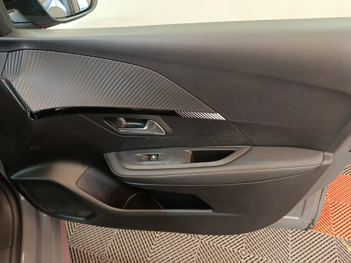 Vue intérieure du panneau de porte côté gauche de la Peugeot 208 gris foncé avec insert effet carbone et commande de vitre.