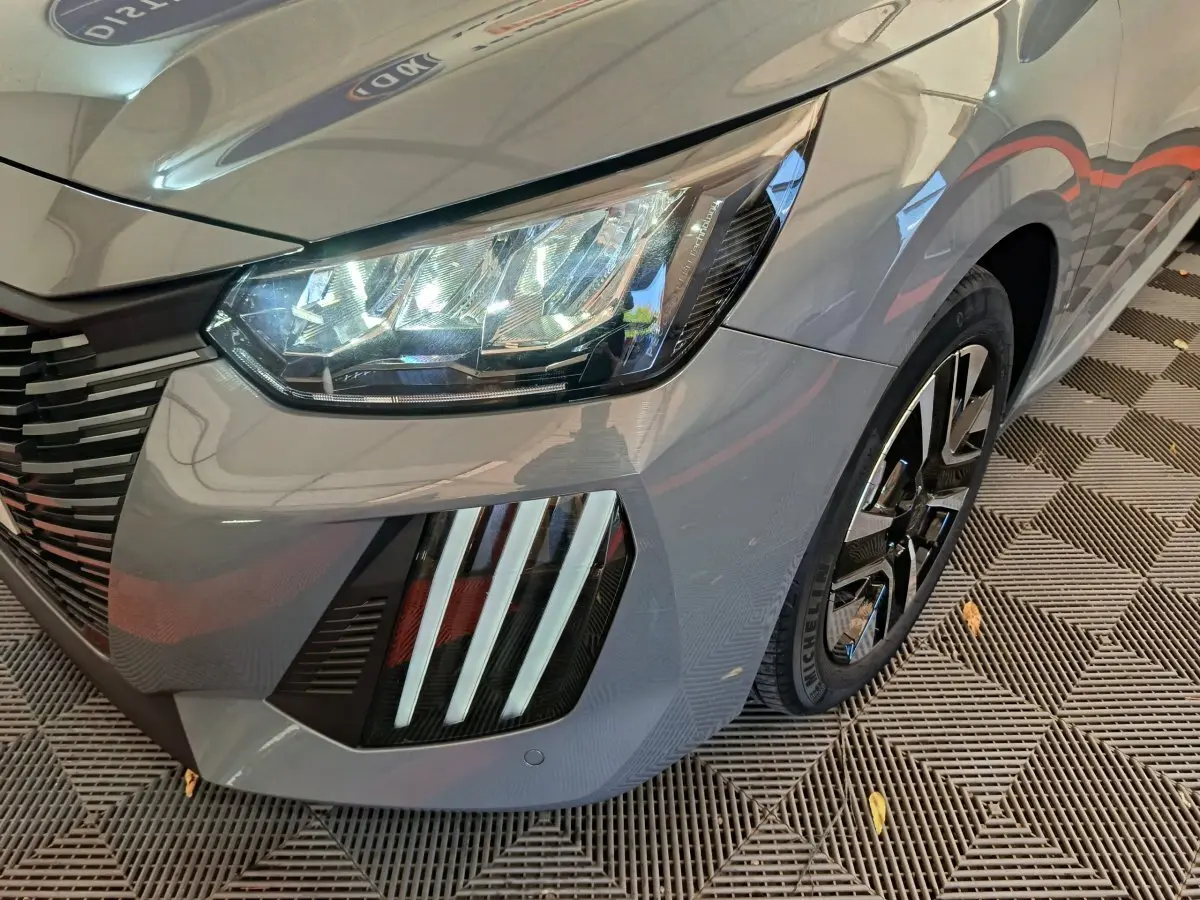 Gros plan sur l'avant droit gris foncé du Peugeot 208 2025, mettant en valeur les phares LED et la calandre distinctive.