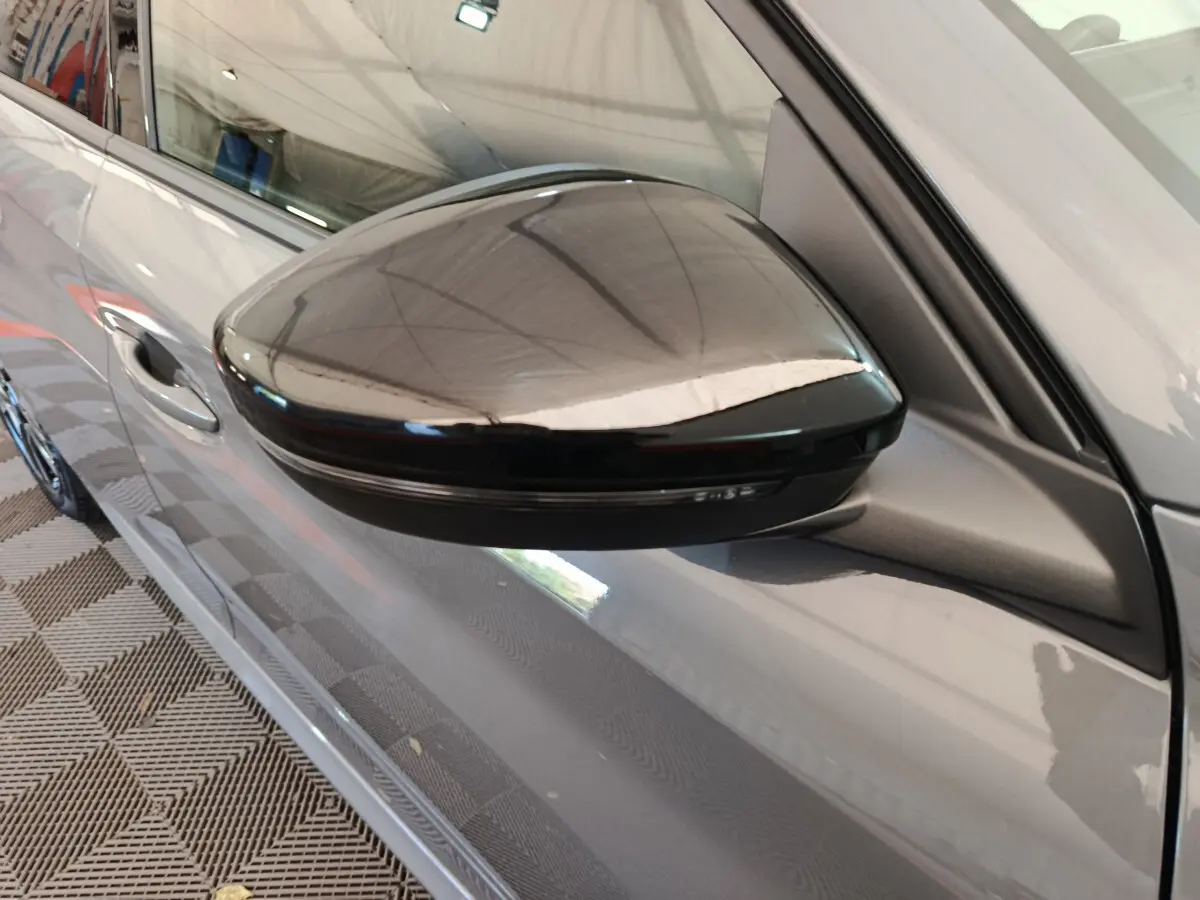 Gros plan sur le rétroviseur droit noir brillant d'une Peugeot 208 gris foncé vue de côté.