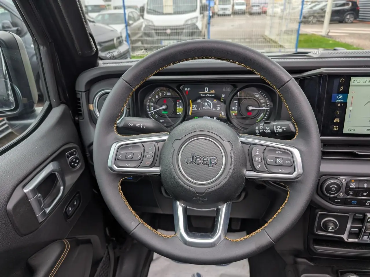Vue intérieure centrée sur le volant noir avec surpiqûres jaunes du Jeep Wrangler 2024, tableau de bord numérique visible.