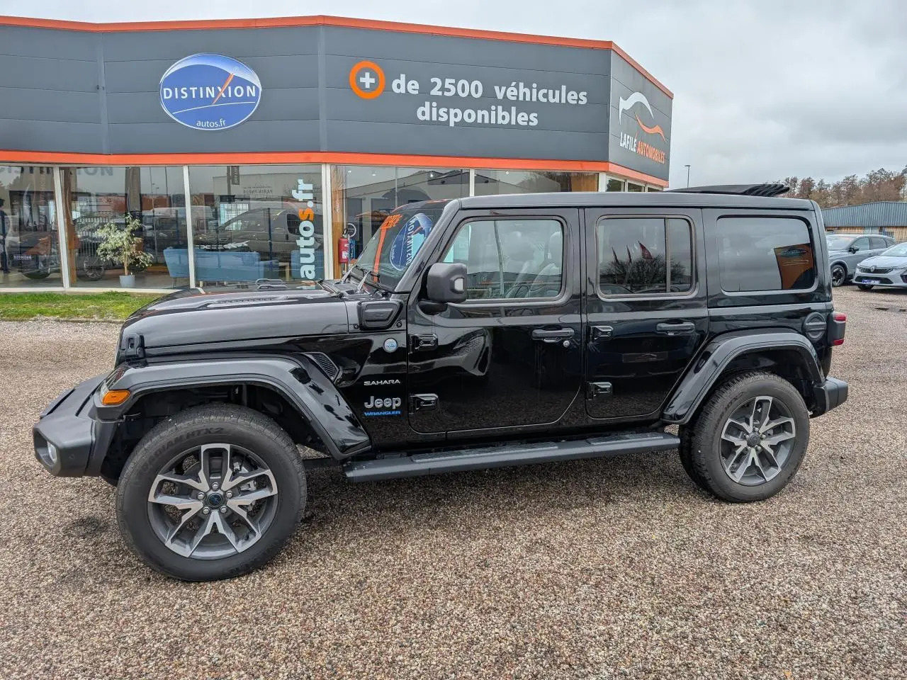 Jeep Wrangler Sahara noir en profil droit, avec jantes alliage 20 pouces et marche-pied visible.