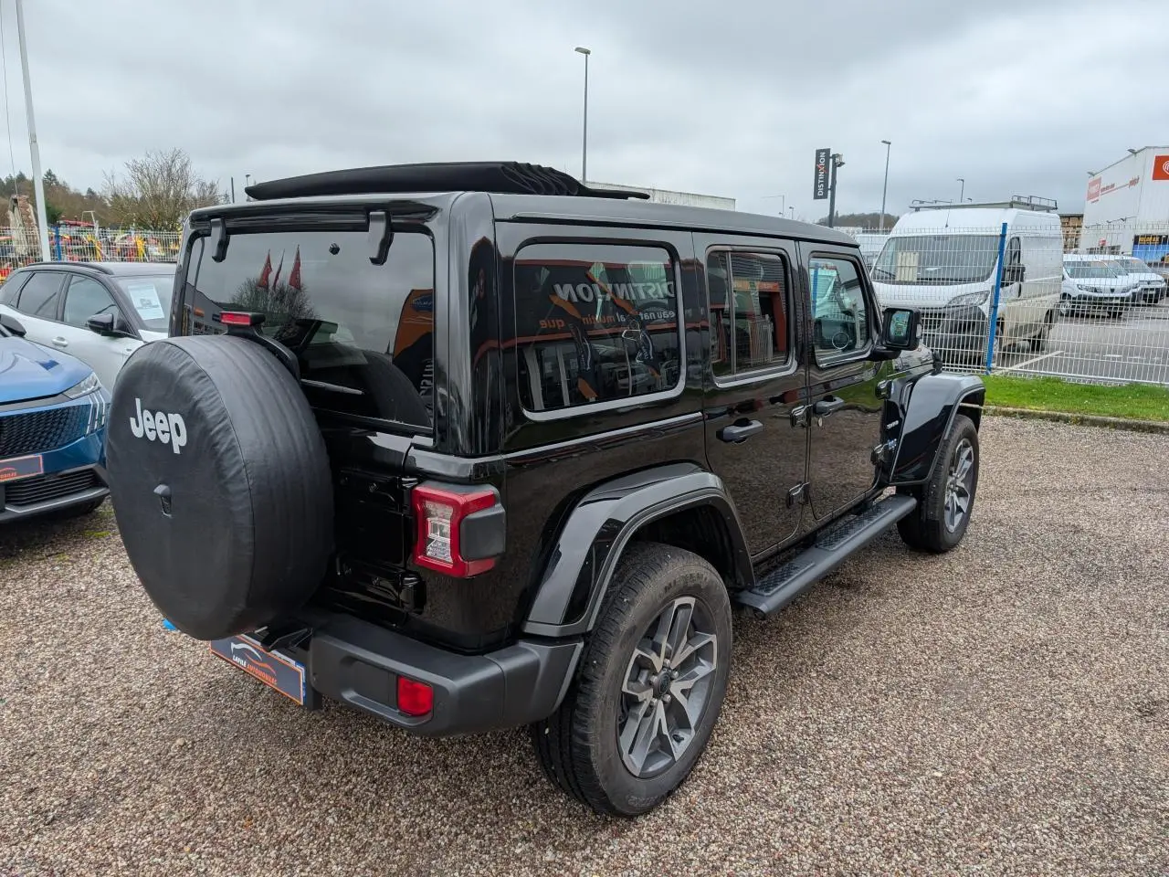 Jeep Wrangler 2024 noir vue 3/4 arrière droit avec roue de secours et marchepied visibles.