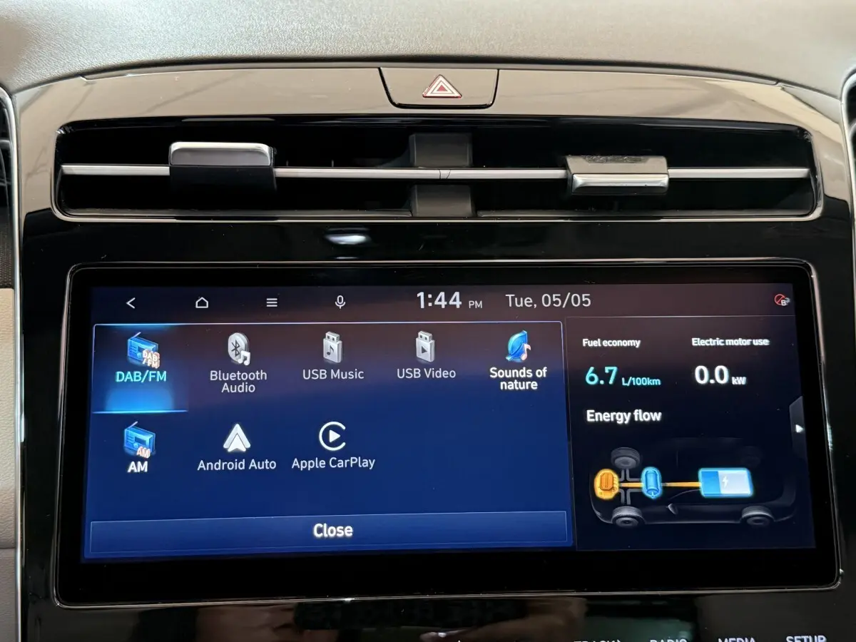 Gros plan sur l’écran tactile central du Hyundai Tucson gris foncé, affichant les options multimédia et consommation hybride.