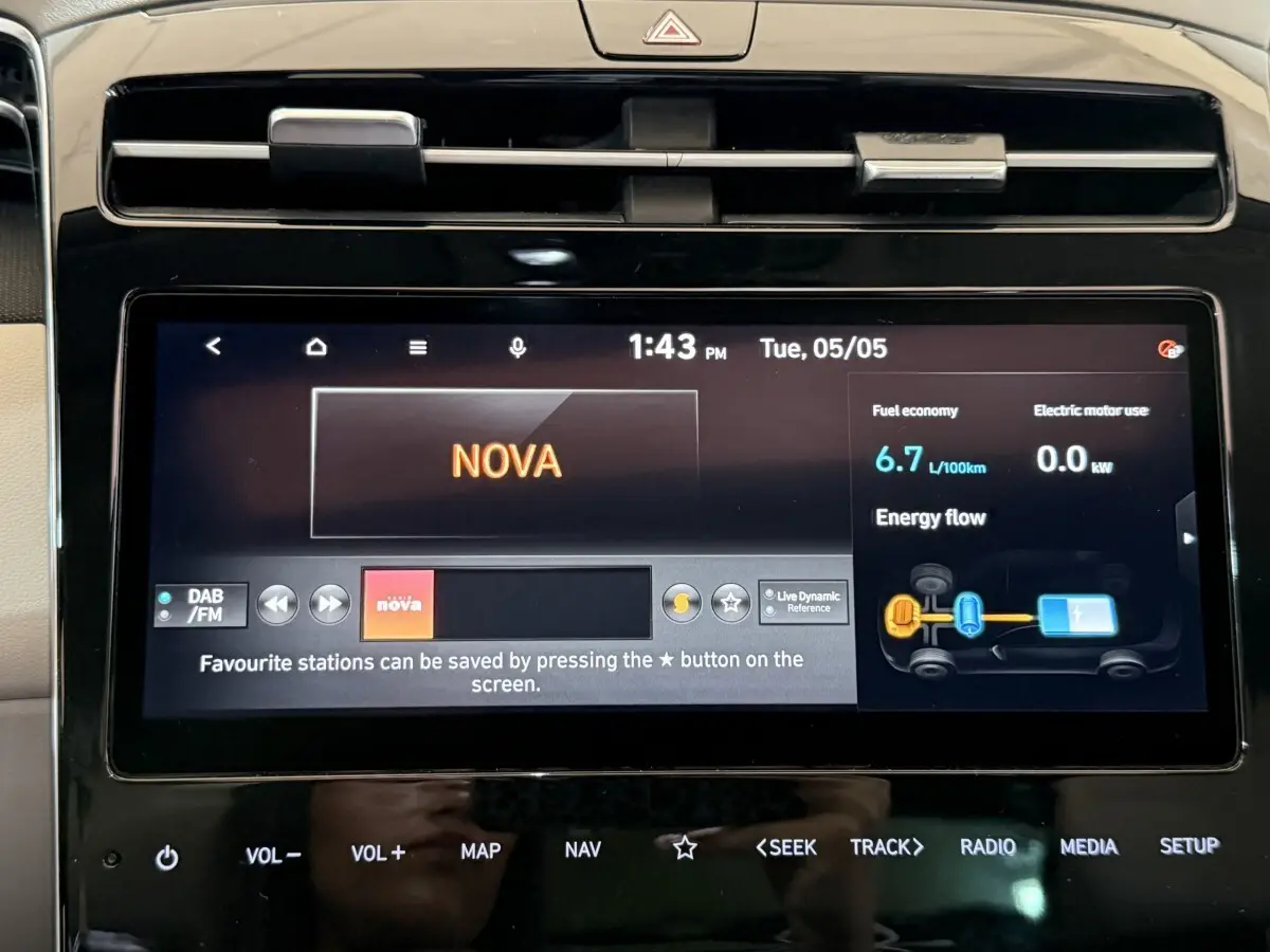 Écran tactile central du Hyundai Tucson gris foncé, affichant radio et consommation hybride, vue intérieure frontale.