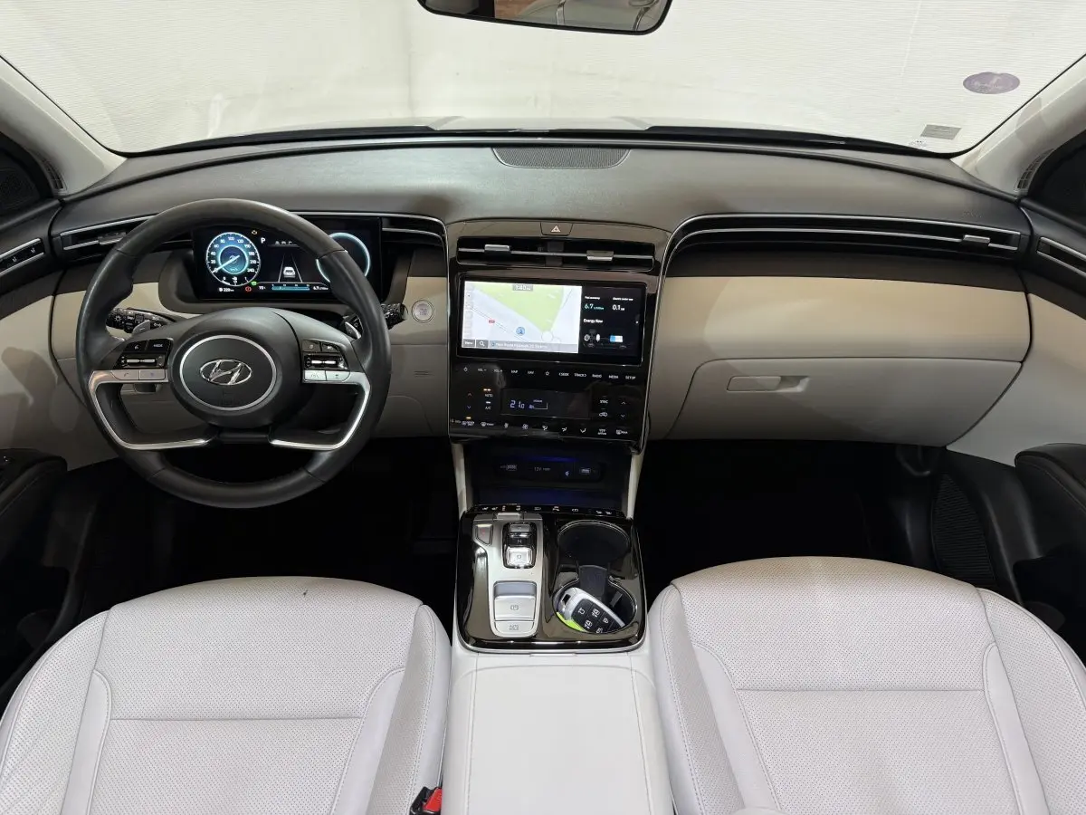 Vue intérieure frontale du Hyundai Tucson 1.6 Hybrid 230 Executive, avec tableau de bord noir et sièges cuir blanc.