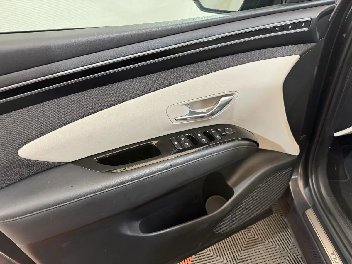 Vue intérieure du panneau de porte avant gauche du Hyundai Tucson gris foncé, avec commandes de vitres et réglages sièges.