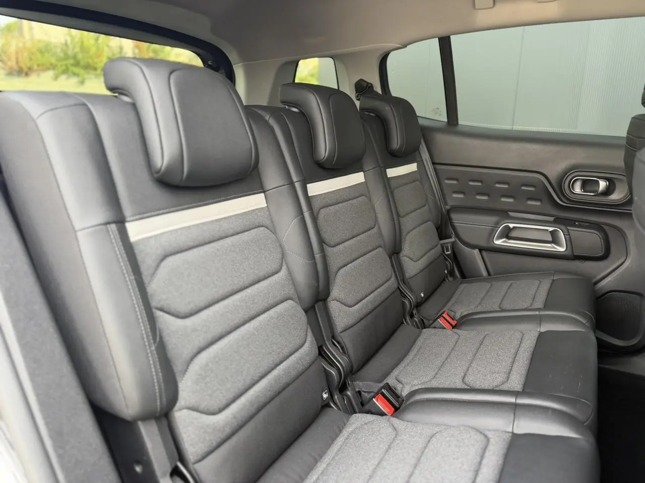 Vue intérieure des trois sièges arrière indépendants gris du Citroën C5 Aircross 2025 avec appuis-tête et ceinture rouge.