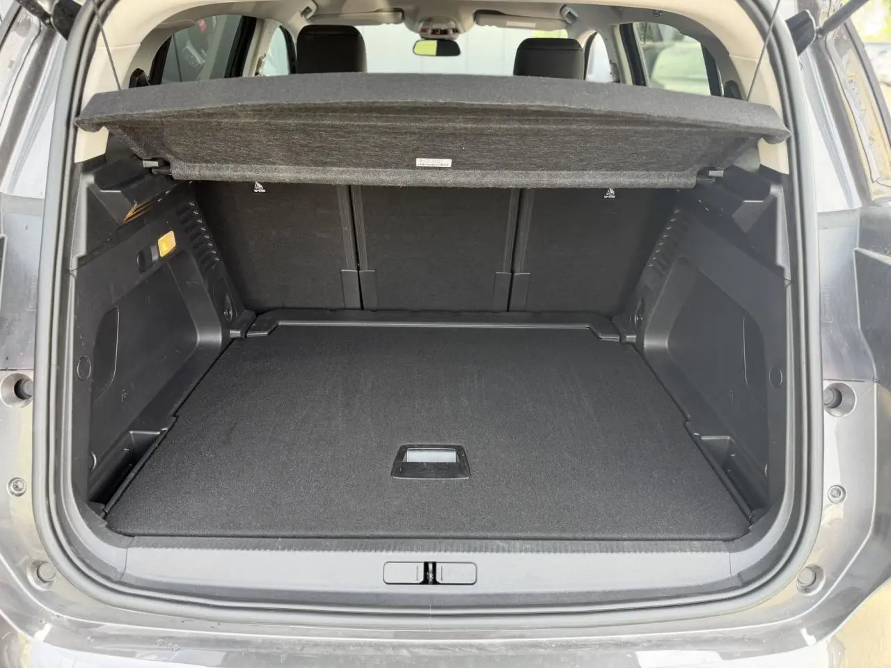 Coffre ouvert vu de l'arrière du Citroën C5 Aircross gris Platinium avec cache-bagages et banquette arrière noire.