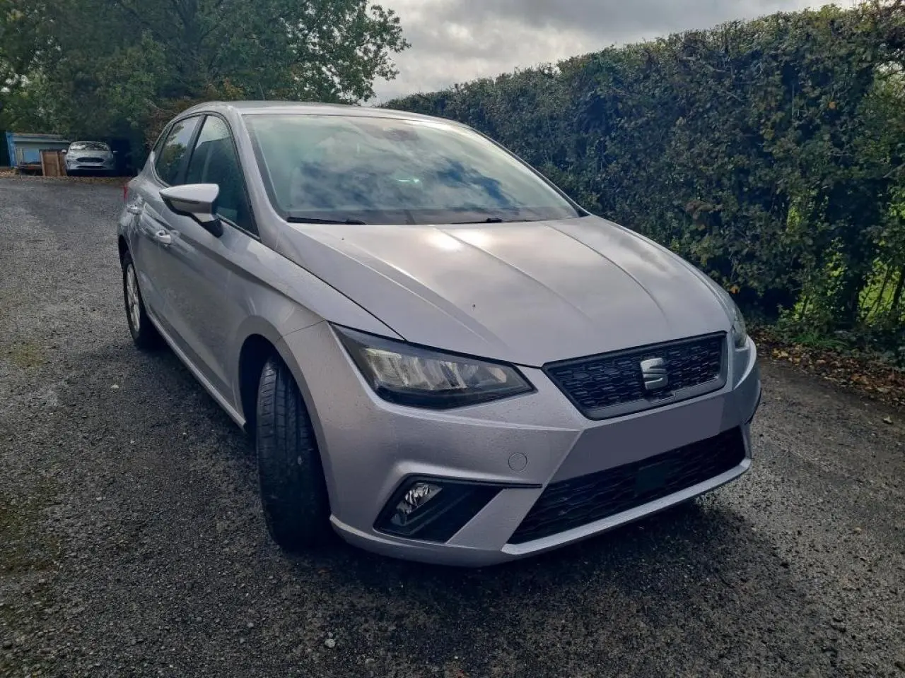 SEAT Ibiza TSI 115 DSG argent urbain vue 3/4 avant gauche sur chemin gravillonné avec haie en arrière-plan