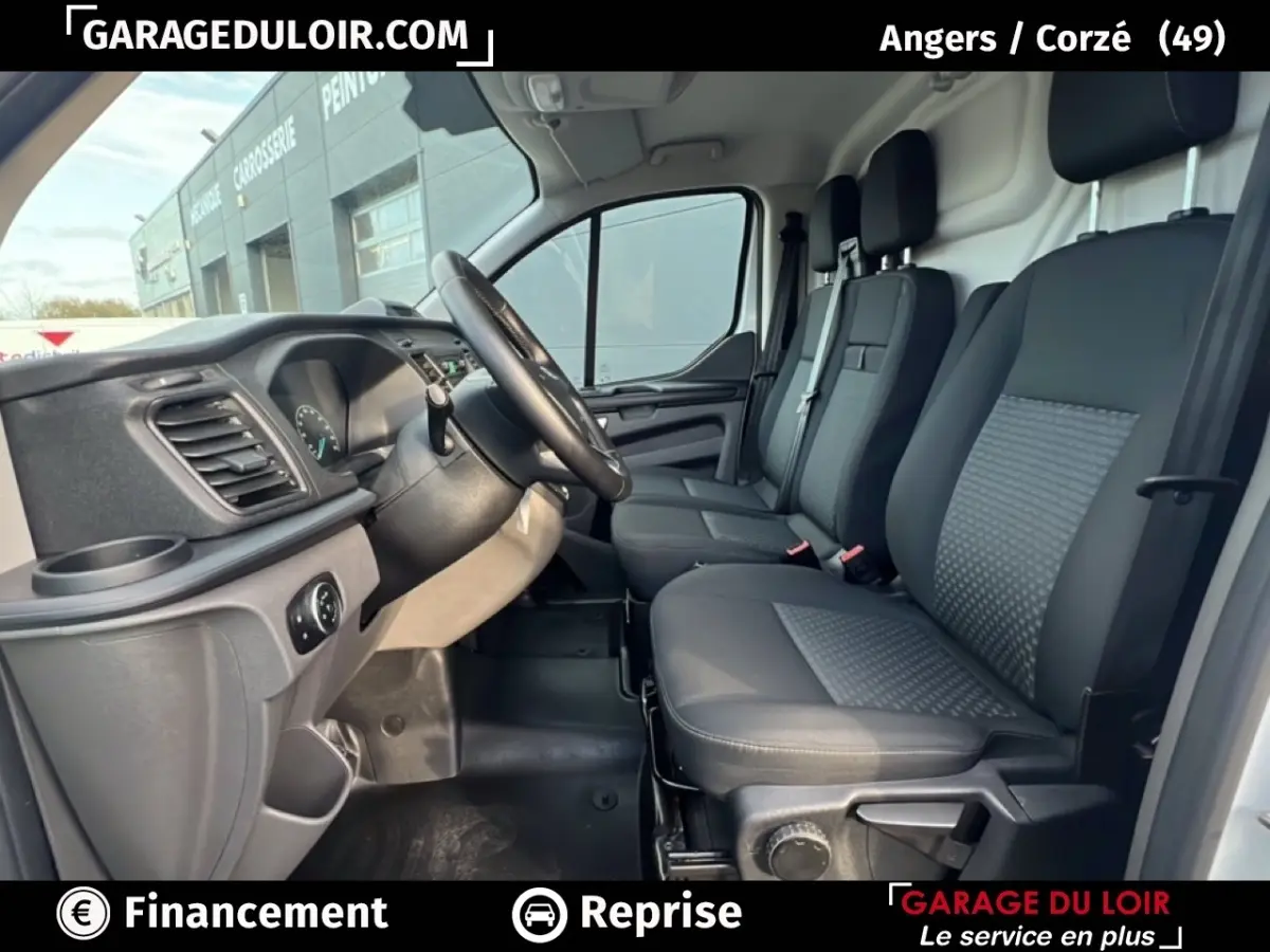 Vue intérieure côté conducteur du Ford Transit Custom Fourgon blanc 2023, montrant les sièges avant et le tableau de bord.