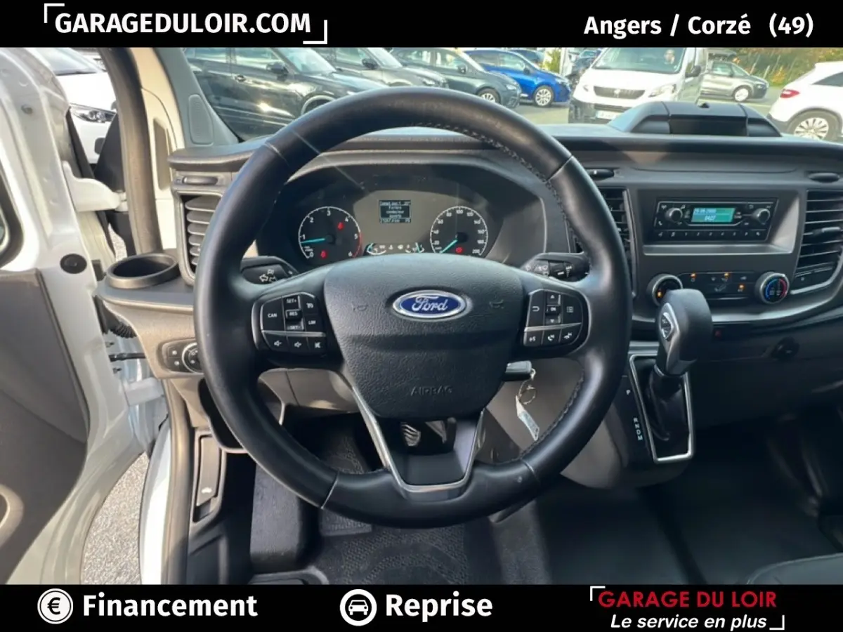 Vue intérieure centrée sur le volant cuir Ford Transit Custom 2023 avec tableau de bord et levier de vitesse automatique visible.