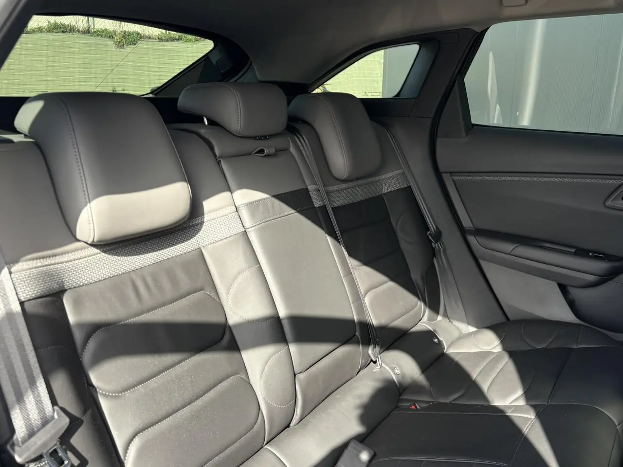 Vue intérieure arrière droite des sièges en cuir noir du Citroën C5 X 2024, avec appuie-têtes et ceintures visibles.