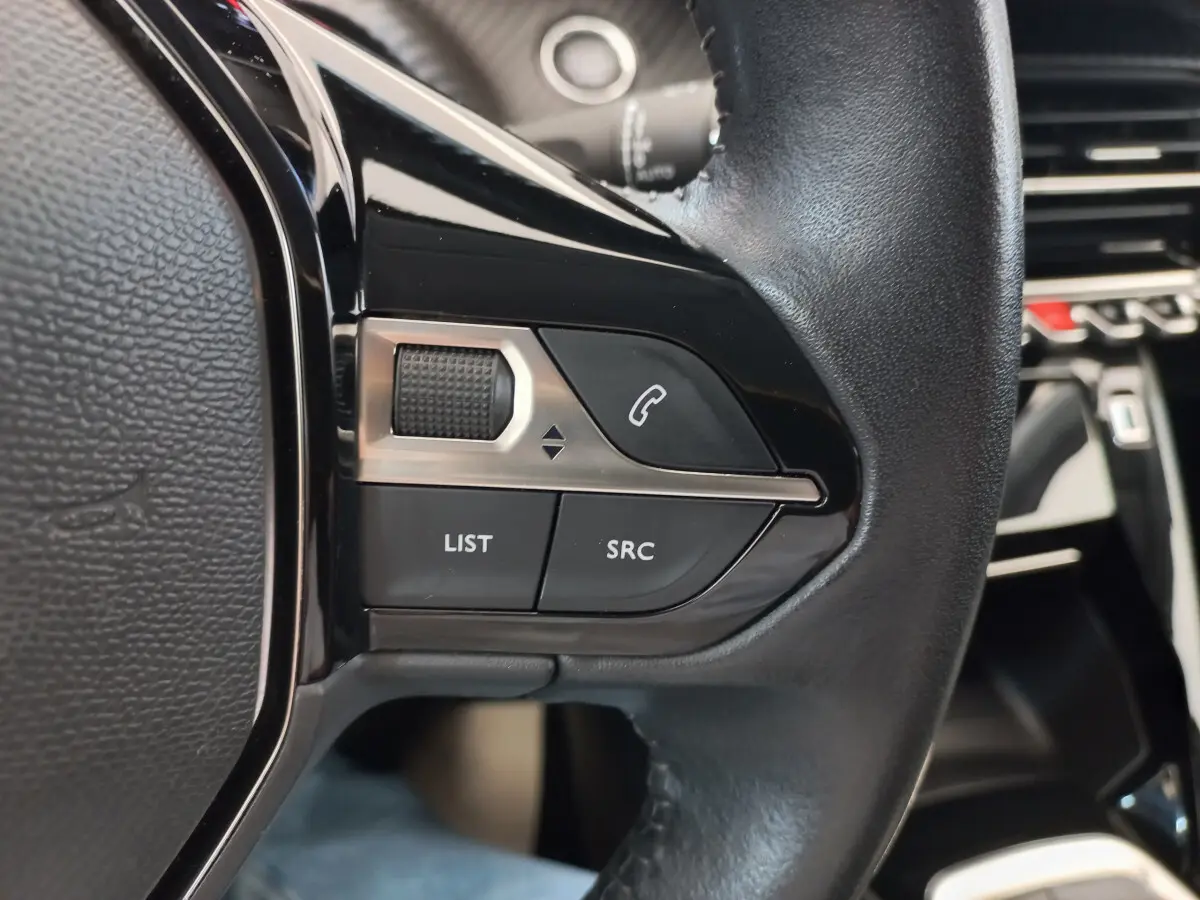 Gros plan sur les commandes noires du volant cuir du Peugeot 208 PureTech 100 S&S Allure 2021, intérieur moderne.