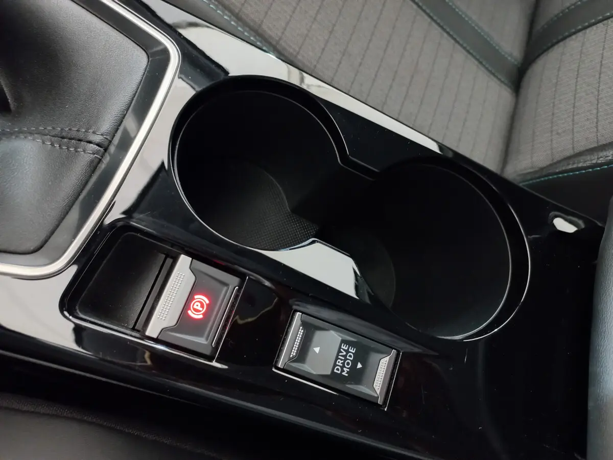 Gros plan intérieur sur la console centrale noire de la Peugeot 208 blanche, avec frein à main électrique et bouton Drive Mode.