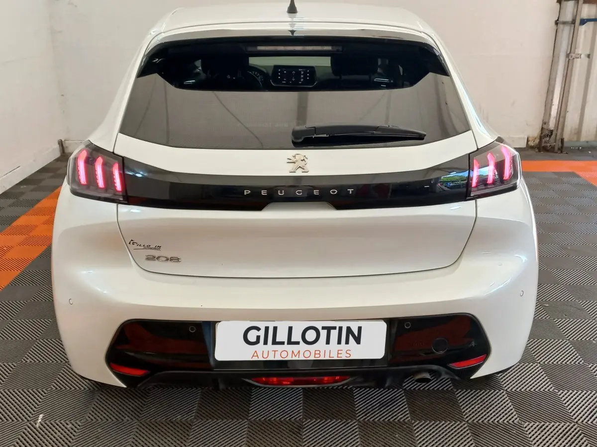 Vue arrière d’une Peugeot 208 blanche de 2021 avec feux LED et logo Peugeot sur bande noire brillante.