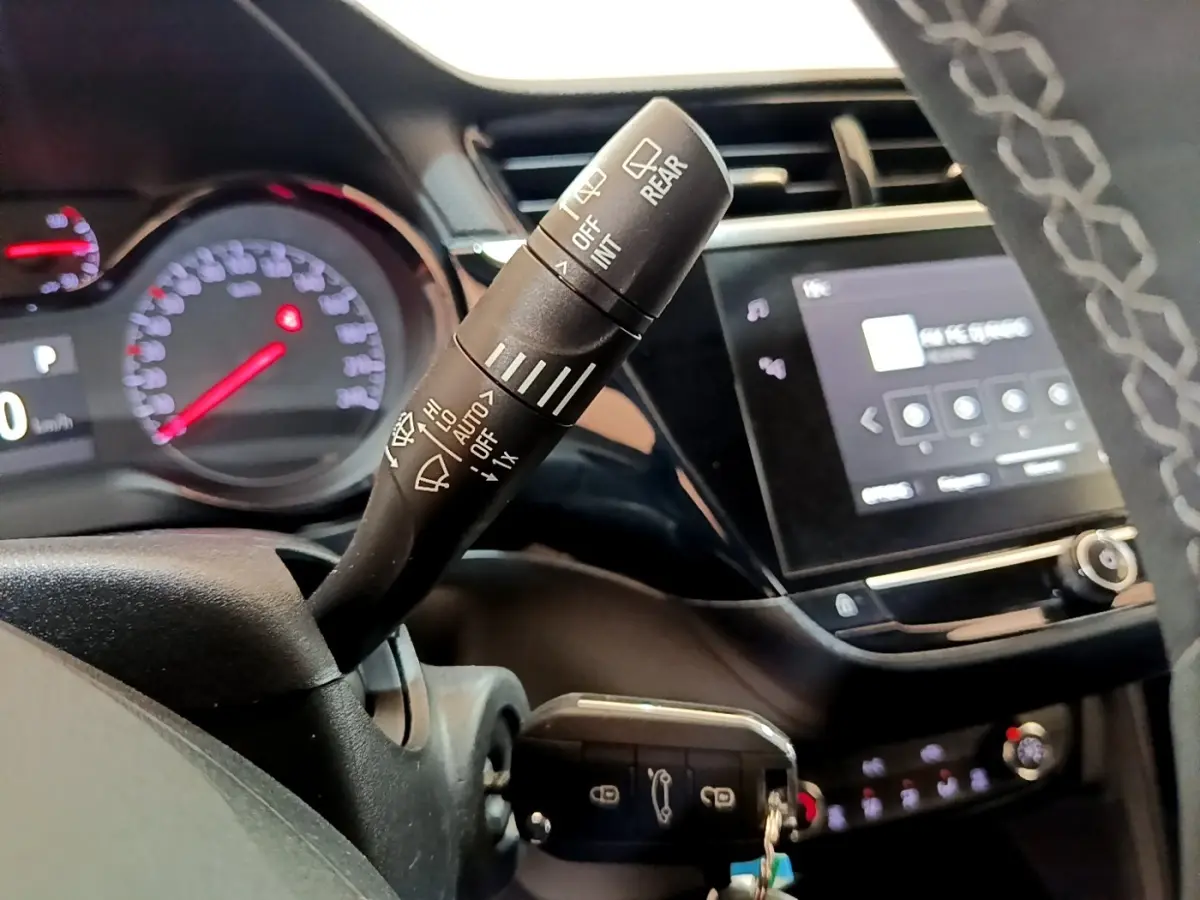 Gros plan sur la commande d’essuie-glace à gauche du volant dans l’habitacle noir de l’Opel Corsa blanche 2023.