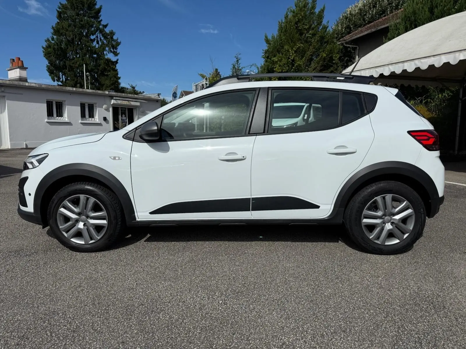 Profil côté gauche d'une Dacia Sandero blanche 2023 avec protections noires et jantes alliage.