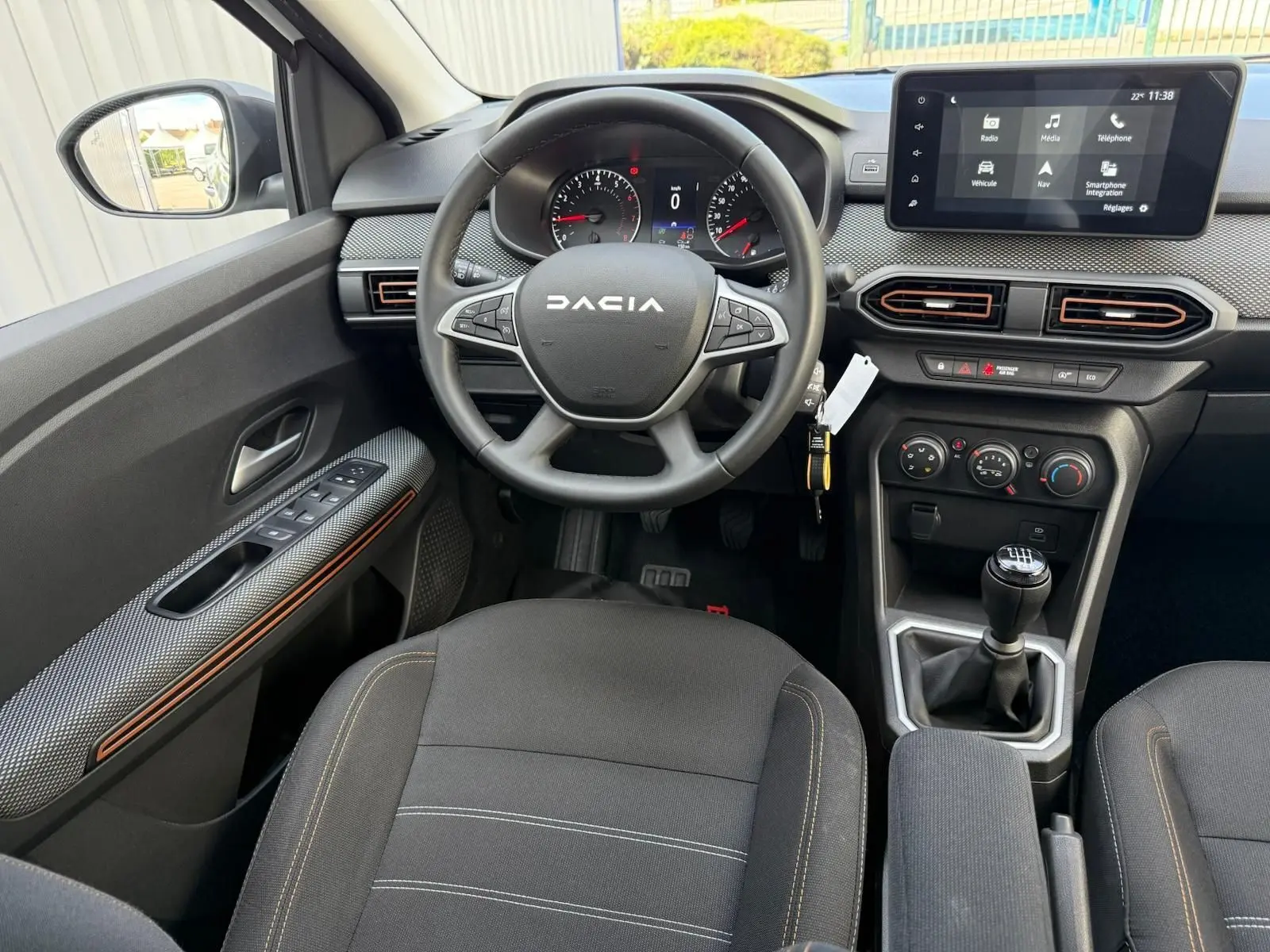 Vue intérieure avant centrée sur le volant DACIA et la console centrale avec écran tactile et boîte manuelle.