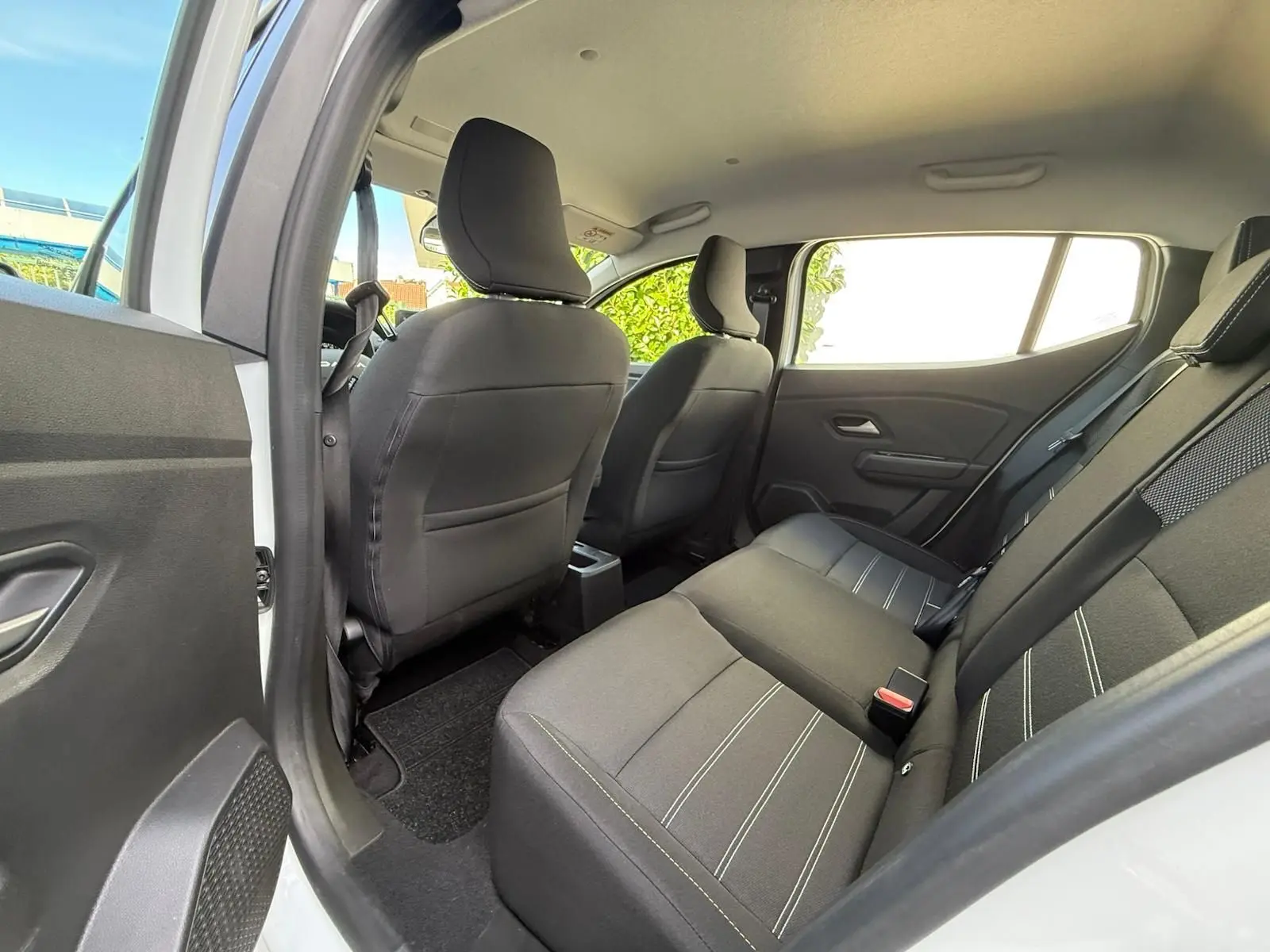 Vue intérieure arrière côté gauche montrant les sièges noirs avec surpiqûres blanches d'une Dacia Sandero blanche 2023.